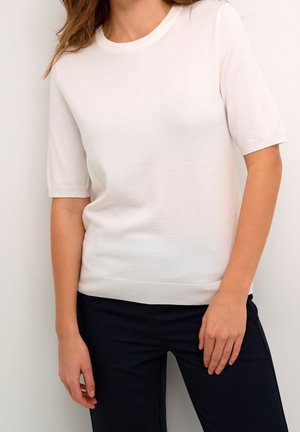 Biały, krótki sweter z krótkim rękawem, okrągłym dekoltem i prążkowanym dołem, połączony z ciemnymi spodniami. Gładka faktura i lekki materiał.