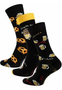 Schwarze Socken mit gelben und orangefarbenen Akzenten, die Muster von Brezeln und Bierkrügen sowie Text zeigen. Strickstoff mit verspielten Designs.