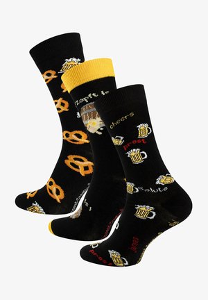 Black socks with yellow and orange accents, featuring pretzel and beer mug patterns and text. Knit fabric with playful designs.