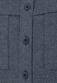 Granatowa koszula o fakturze, z dwiema kieszeniami na piersi i ciemnymi guzikami, z widocznym splotem i dopasowanym krojem.