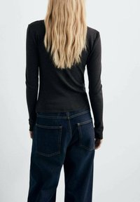 Langdonige zwarte top met een fitted ontwerp, gecombineerd met losse donkerblauwe jeans met twee achterzakken en zichtbare stiksels.