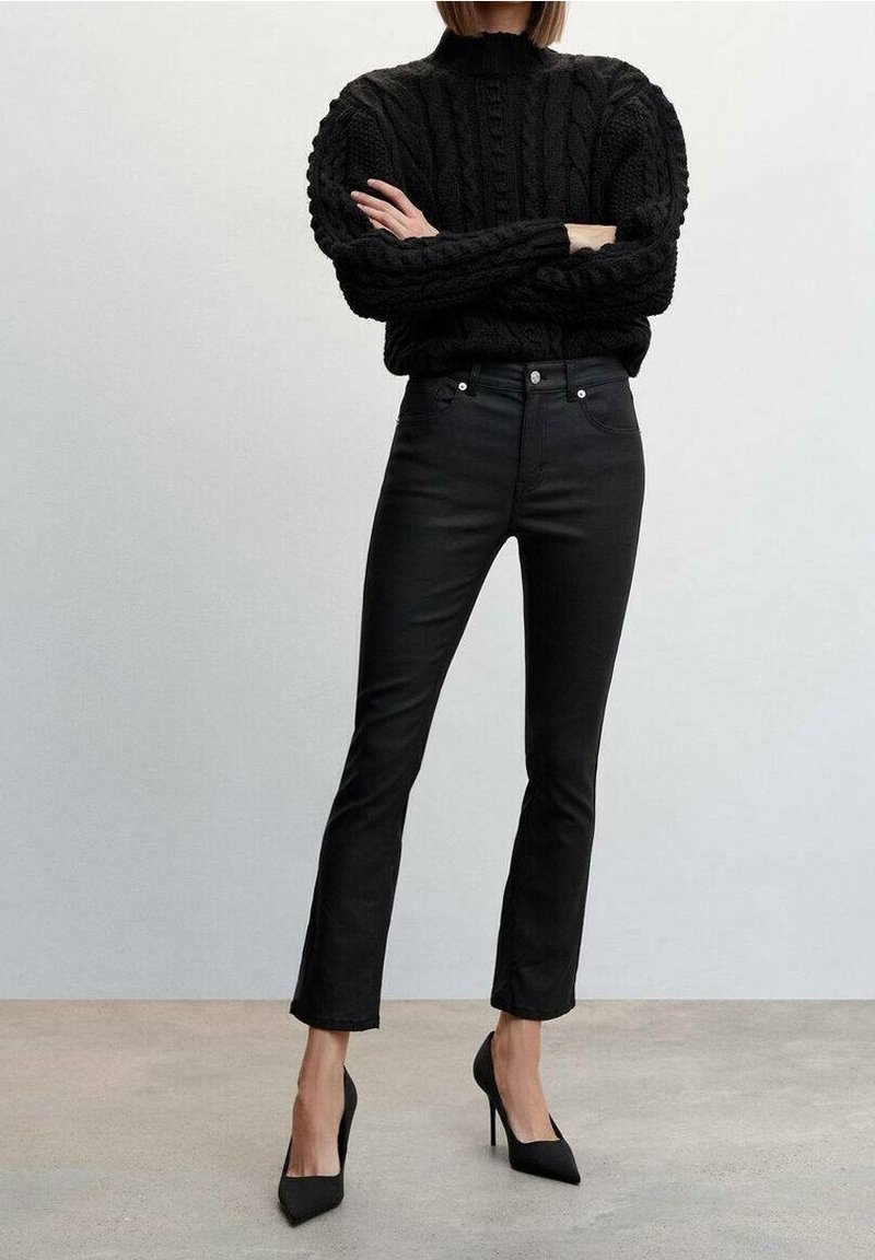 Černý pletený svetr s vysokým límcem a texturovaným vzorem, spárovaný s úzkými černými džínami a špičatými černými lodičkami.
