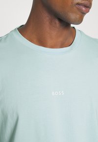 Ljust blå t-shirt med kort ärm, tillverkad av mjuk tyg med rund halsringning. Har texten "BOSS" i vitt på bröstet.