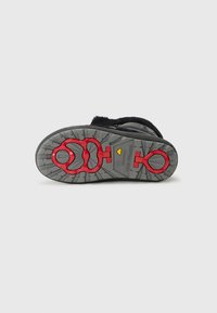 La semelle de la chaussure présente une surface grise texturée avec un motif circulaire rouge, spécialement conçue pour l'adhérence et la traction sur divers terrains.