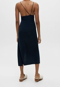 Robe sans manches bleu marine avec de fines bretelles, longueur midi et texture lisse ; associée à des sabots à talons blocs clairs.