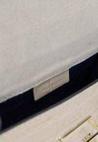 Krémová kožená kabelka s textured povrchem, zlatým kováním a vnitřní štítkem s nápisem "pravá kůže, vyrobeno v Itálii." Podšívka z tmavé látky.