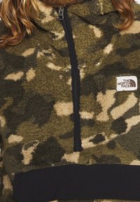 Sudadera polar en camuflaje verde, con cierre de cremallera negro y bajo elástico negro. Tela texturizada con forro interior suave.