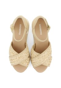 Sandalias beige con un diseño de tiras trenzadas y una superficie texturizada. Una hebilla dorada acentúa la correa del tobillo. Suela plana, simple y minimalista.