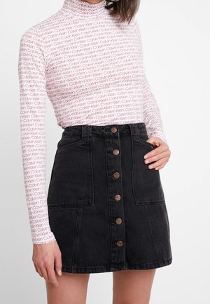 Langarm top met hoge hals en herhalend rood "Calvin Klein" logo op een lichtroze achtergrond, gecombineerd met een zwarte denim rok met knopen aan de voorkant.