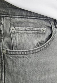Grijs denim jeans hebben een voorzak met zilverkleurige hardware, contrasterende stiksels en een gestructureerde stof die zichtbaar is langs de naden.