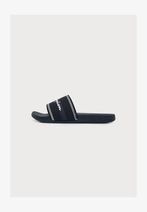 Sandalo nero tipo slide con ampia fascia di tessuto con strisce bianche e testo parziale del logo bianco, mostrato su uno sfondo chiaro e uniforme.