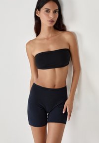 Top bandeau nero senza cuciture abbinato a pantaloni corti neri a vita alta, realizzati in un tessuto liscio ed elastico. Design semplice e aderente senza motivi.