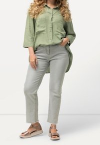 Lichtgroene linnen overhemd met twee borstzakken, gecombineerd met lichtgrijze denim broek en bronzen plateau sandalen met een strap.