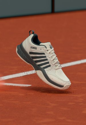 Valge ja must K-Swissi tennisesaabas tõstab punasel savitenniseväljakul valge joone lähedal üles savi tolmu.