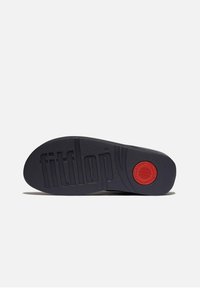 Zwarte rubberen zool van een schoen met een verhoogd "fitflop" logo, gestructureerd oppervlak en een rode cirkelvormige accent nabij de hak.
