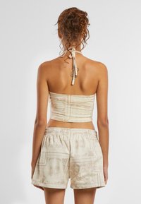 Kreemist halter-topist, millel on mustriline disain, koos sobivate lõdva lõikega lühikeste pükstega, millel on elastne vöökoht. Pehme kangast tekstuur.