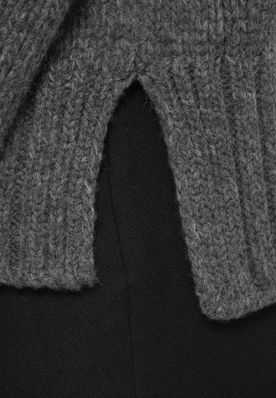 Primo piano di un tessuto grigio a maglia sovrapposto con texture a coste su un tessuto nero liscio, mostrando dettagliati modelli tessili.
