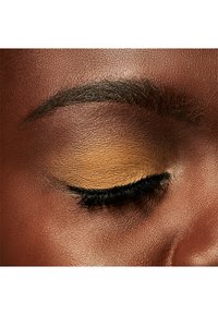 Close-up van een gesloten oog met gouden oogschaduw, zwarte wimpers en goed verzorgde wenkbrauw op gladde, donkere huid.