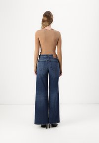 Un haut marron à manches longues associé à un jean en denim bleu foncé, ample et taille haute, avec des poches arrière et une étiquette de marque sur la ceinture.