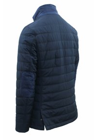 Giacca trapuntata navy con colletto alto, texture liscia e toppe sui gomiti. Vestibilità slim con orlo leggermente curvato sul retro.