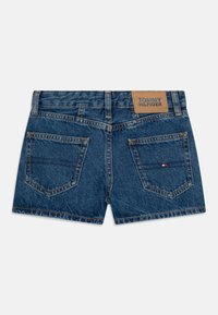 Džínové šortky se středním modrým odstínem, tradičními zadními kapsami a koženou nášivkou s logem "TOMMY HILFIGER" na pase.
