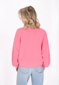 Sudadera oversized rosa con hombros caídos, puños y dobladillo acanalados. Combinada con jeans de un azul claro, que muestran un ajuste relajado.