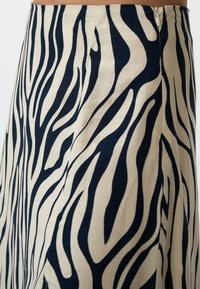Une jupe beige avec un motif rayé zèbre bleu marine. Elle dispose d'une fermeture éclair sur le côté et d'une texture lisse en lin. Design évasé à l'ourlet.