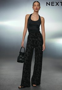 Top negru fără mâneci, cu decolteu rotund, asortat cu pantaloni largi cu talie înaltă, negri, cu un model, și o geantă mică neagră.