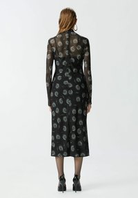Crna midi haljina s dugim prozirnim rukavima, koja ima uzorak spirale u srebrnoj boji. Glatka tkanina, oblinasti dizajn, zatvaranje na patentni zatvarač na leđima.