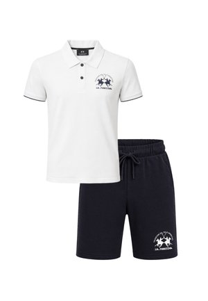 Polo bianca a maniche corte con bottoni neri e logo abbinata a pantaloncini neri con coulisse con logo in tinta sulla gamba sinistra.