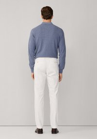 Suéter azul de punto con cuello, combinado con pantalones blancos y zapatos oscuros, visto desde atrás contra un fondo claro.