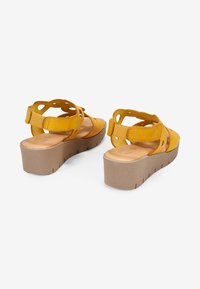 Sandalias de plataforma amarillas con un acabado suave, talón abierto y detalles recortados en las correas. Suela beige texturizada con ranuras.