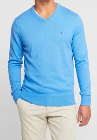 Hellblauer V-Ausschnitt-Pullover aus weichem Strickmaterial, mit gerippten Bündchen und Saum sowie einem kleinen Logo auf der linken Brust.