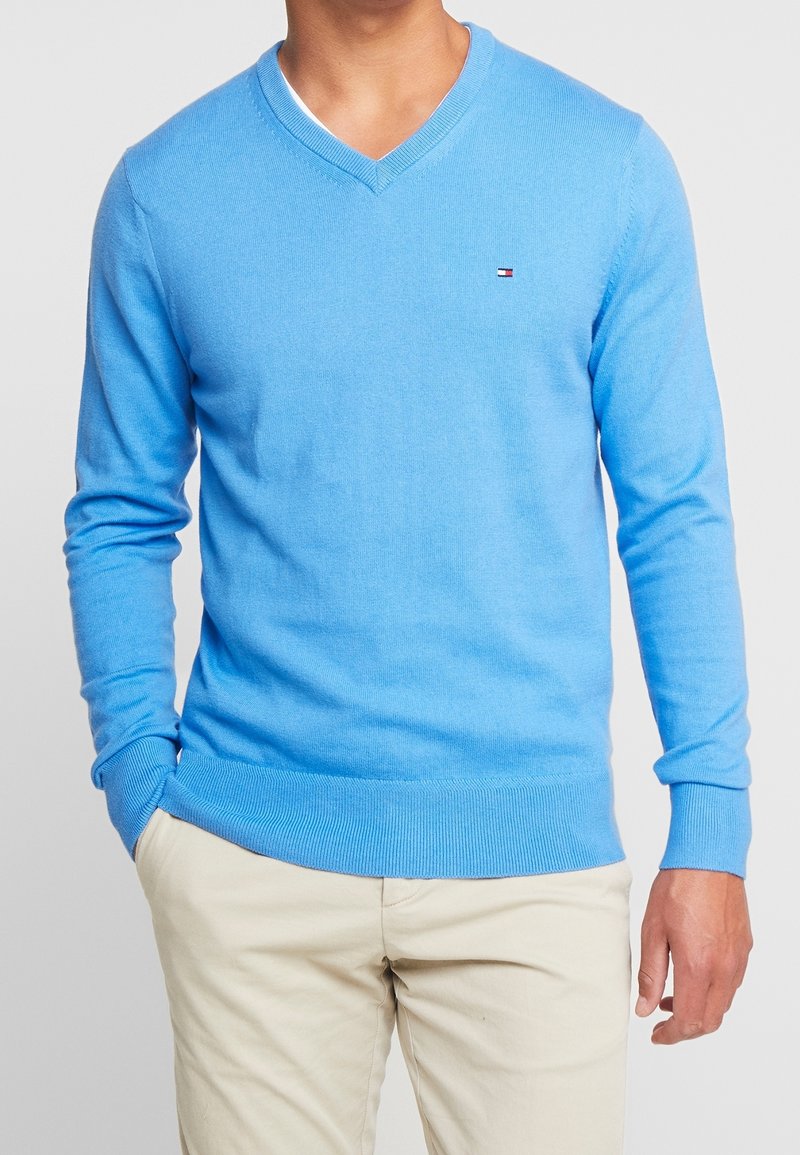 Hellblauer V-Ausschnitt-Pullover aus weichem Strickmaterial, mit gerippten Bündchen und Saum sowie einem kleinen Logo auf der linken Brust.