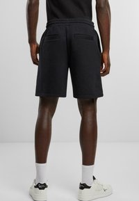 Black sweat shorts made from soft fabric, featuring an elastic waistband, back pockets, and a casual cut, paired with white sneakers and socks.