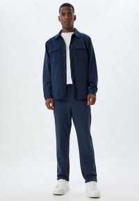 Marineblåt afslappet outfit bestående af en skjorte med knapper og to forlommer samt matchende sweatpants. Glat stof med en afslappet pasform.