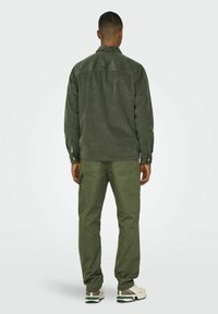Chaqueta de camisa de pana en verde oliva con dos puños abotonados; combinada con pantalones cargo en verde oliva que cuentan con múltiples bolsillos y un ajuste relajado.