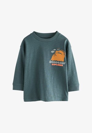 Chemise à manches longues verte en tissu doux, ornée d'un graphique de dinosaure orange avec le texte "Explorateur de dinosaures" en blanc en dessous.
