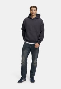 Mörkgrå hoodie med känguruficka och dragsko, worn över en vit skjorta. Kombinerad med blå jeans och marinblå sneakers med vita ränder.