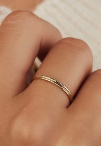Bague en or avec une finition lisse et polie, présentant un design fin et délicat. Portée sur une main à la peau claire.