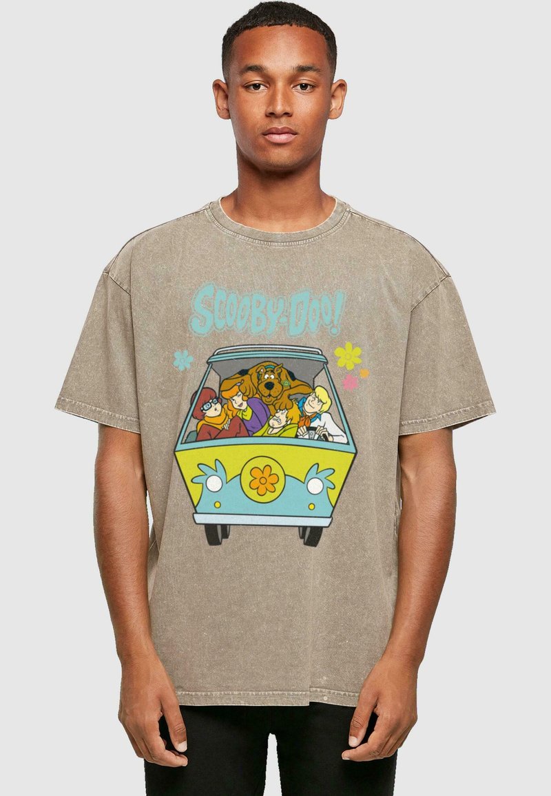 Camiseta de algodón color beige con un impreso colorido de "Scooby-Doo!" que muestra a los personajes en una furgoneta, con un diseño de flores amarillas en el vehículo.