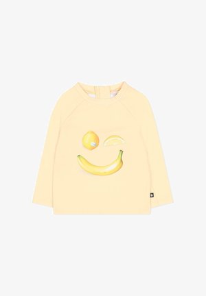 Lichtgele blouse met lange mouwen, met een citroen, citroenschijfje en banaan gerangschikt als een glimlachend gezicht op de voorkant.
