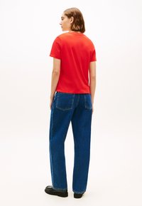 T-shirt di cotone rossa con maniche corte, abbinata a jeans di denim blu a vita alta. L'outfit presenta una vestibilità comoda e colori solidi.