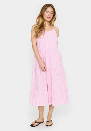 Robe maxi rayée rose et blanche avec un design à volants, des bretelles spaghetti réglables et une coupe ample, assortie à des tongs noires.