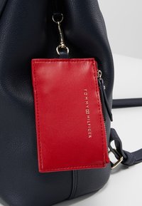 Zaino in pelle blu navy con finitura testurizzata, dotato di porta carte rosso rimovibile con logo in rilievo e accenti in hardware dorato.