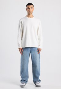 Lange mouw off-white shirt en lichte blauwe, losse spijkerbroek met een gemiddelde taille, gedragen met witte en grijze sneakers. Eenvoudige, casual outfit.