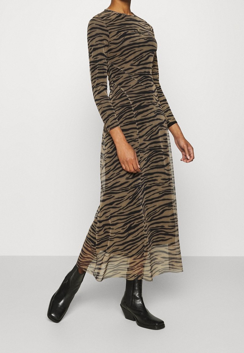 Femme portant une robe longue à manches longues, longueur cheville, à rayures tigre, associée à des bottines noires.