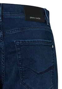 Achterzak en tailleband van donkerblauwe denim jeans met een zwart leren label "pierre cardin" aan de achterkant.