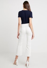 Marinblå ribbat kortärmad toppen kombinerad med vita utsvängda byxor, med kontrasterande sömmar och klackar med ankelrem, sedd bakifrån.