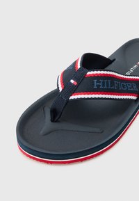 Navy flip-flop featuring a textured sole, fabric thong strap with red and white accents, and logo embroidered in blue.
